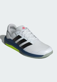 Zapatilla deportiva blanca con diseño de tres rayas negras, parte superior de malla, punta redondeada, suela azul y acentos verdes en la suela exterior.