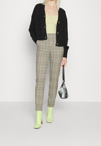 Černý pletený cardigan, světle zelený top, kostkované béžové kalhoty, mátově zelené kotníkové boty a taška s černo-bílým vzorem.