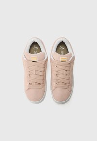 Baskets en suède rose avec des accents blancs, présentant un design de lacets épais, des semelles en caoutchouc et une petite étiquette de logo sur la languette.