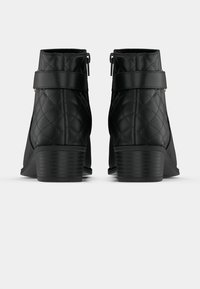 Črni gležnjarji iz prešitega sintetičnega materiala, z bočnim zadrgo, trakastim poudarkom in strnjenim peto.