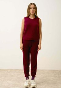 Bordeauxstickad ärmlös topp i kombination med matchande åtsittande träningsbyxor, med ribbat mönster och elastiska mudd, kompletterad med vita sneakers.