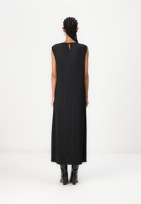 Rochie neagră plisată cu decolteu tip clemă, design fără mânici și siluetă fluidă, asortată cu botine negre lucioase până la gleznă.