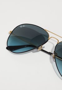 Ray-Ban aviator sunglasses with dark blue lenses, thin gold metal frame, and clear nose pads, featuring a minimalist design and rounded shape.