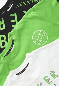 Tre t-shirts: sort med grøn tekst, lys grøn med cirkulært logo, og hvid med grøn skrift. Bomuldsstof, rund hals design.