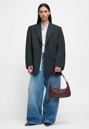 Veste oversize gris foncé portée sur une chemise bleu clair, associée à un jean bleu à jambes larges et un sac à main en cuir bordeaux. Chaussures noires à bout pointu.