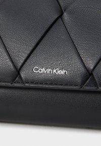 Borsa in pelle nera con motivo trapuntato, texture liscia e logo "Calvin Klein" in argento in basso a destra.