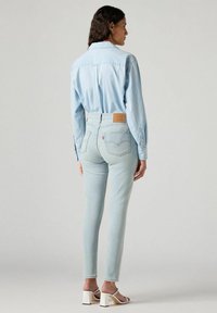 Vaqueros de mezclilla azul claro con una cintura alta, bolsillos traseros y una etiqueta de cuero marrón en la cintura. Combinados con una camisa de botones azul claro.