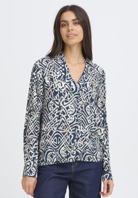 Blouse à manches longues en navy et crème avec des motifs abstraits. Comprend un col, une patte de boutonnage et une coupe décontractée. Texture de tissu lisse.