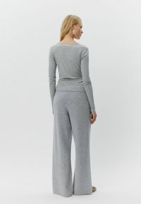 Graues Langarmoberteil und weite Hose aus weichem Stoff, mit einem lässigen Schnitt und minimalistischem Design. Glatte Textur ohne Muster.