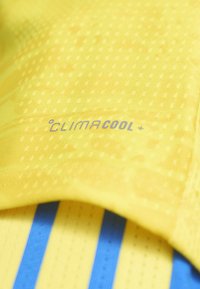 Tissu jaune avec de petites perforations et des rayures bleues en dessous, comportant le texte "CLIMACOOL+" imprimé à la surface.
