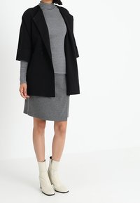 Svart oversize-kappa, randig polotröja, grå kjol och krämsfärgade ankelskor. Slät tyg, rena linjer och minimal dekoration.