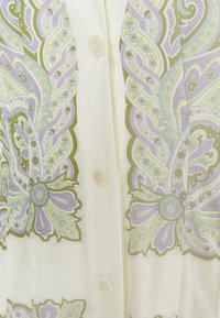 Tissu crème avec des motifs floraux paisley complexes en vert, lavande et bleu clair, et trois petits boutons translucides le long du centre.