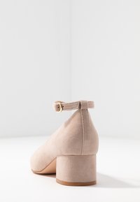 Scarpa con tacco alto in suede beige, con punta arrotondata e tacco spesso, dotata di una cinghia alla caviglia sul retro con dettaglio della fibbia dorata.