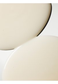 Twee overlappende ronde borden, glad crème-kleurig keramiek met een glanzende afwerking. De randen hebben een subtiele zwarte omtrek.
