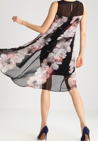 Černé bezramenné šaty s volným průsvitným přehozem, zdobené velkými růžovými a bílými květinovými vzory. Klíčová výřez na zadní straně.
