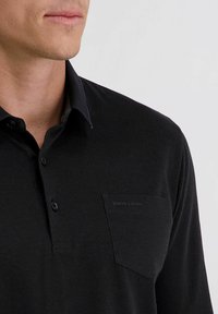 Schwarzes Langarm-Polohemd mit Kragen, ausgestattet mit einer Brusttasche, die mit "pierre cardin" geprägt ist, aus einem glatten, strukturierten Stoff.