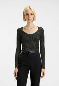 Top nero a maniche lunghe con scollatura a barco e texture a coste, caratterizzato da fili metallici, abbinato a pantaloni neri sartoriali e una cintura.