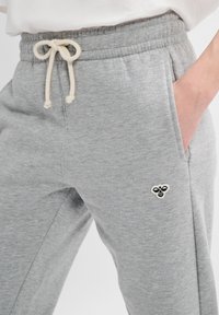 Grijze katoenen joggers met een trekkoord in de taille, zijzakken en een klein zwart en crèmekleurig bijenlogo op de dij. Zachte textuur, casual pasvorm.