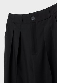 Pantalon noir avec une ceinture à boutons, des plis, et une finition en tissu lisse présenté sur un fond uni.