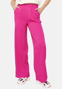 Roze, wijde broek met een textuurstof, elastische tailleband en zijzakken, gedragen met witte sneakers met zwarte accenten.