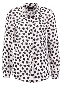 Weiße Bluse mit langen Ärmeln, die ein schwarzes herzförmiges Muster, eine durchgehende Knopfleiste und einen klassischen Kragen aufweist. Aus glattem, leichtem Stoff gefertigt.