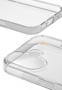 Průhledný kryt na smartphone s zaoblenými hranami, výřezem na kameru ve tvaru srdce a vyraženým textem "IDEAL OF SWEDEN." Hladký, průhledný plastový povrch.