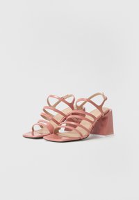 Pink patent leather sandals featuring multiple crisscross straps, open toe, and square block heel with a glossy finish.