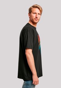 Zwarte katoenen t-shirt met een kleurrafie van bergen in tinten van rood, paars en turquoise, met een relaxte pasvorm en korte mouwen.