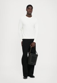 Pulover alb cu nervuri, cu mâneci lungi, asociat cu pantaloni negri largi. Ținând o geantă neagră texturată cu accente aurii.