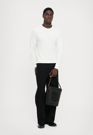 Witte geribde trui met lange mouwen, gecombineerd met zwarte wijde broeken. Houdt een zwarte tas van textuur met gouden accenten vast.