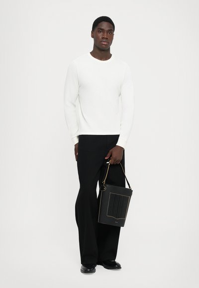 Un pull blanc à côtes avec des manches longues, associé à un pantalon noir à jambes larges. Tenant un sac noir texturé avec des accents dorés.