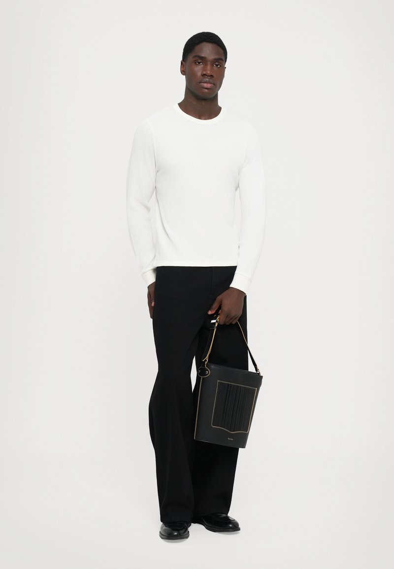 Balta ribota džemperis ar garām piedurknēm, pāris ar melniem platiem biksēm. Tur rokā melnu teksturētu somu ar zelta akcentiem.