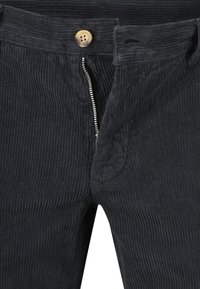 Zwarte corduroy broek met een gedeeltelijk open zilveren rits en een bruine knop boven de gulp.