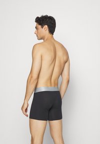 Black boxer briefs made of smooth fabric with a wide gray elastic waistband, fitted design, and short legs, viewed from the back.