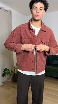 Veste en velours côtelé à carreaux rouges avec un design à boutons, deux poches poitrine et une coupe décontractée. Portée sur une chemise blanche et un pantalon noir.