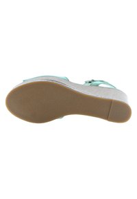 Korokenkä, jossa on säädettävä turkoosi hihna, teksturoitu harmaa yläosa ja ruskea kumipohja. Siinä on huomaamaton metallinen yksityiskohta reunan varrella.