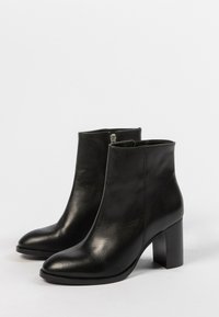 Une paire de bottines en cuir noir avec des talons blocs et des fermetures éclair sur les côtés, sur un fond clair.
