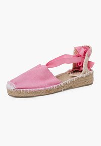 Rožinės kanvasinės espadrilės su džuto padu. Yra atviras kulnas, plokščias dizainas ir dekoratyvios kaspinų pynės ant kulno. Baltos siūlės detalės.