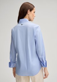 Camicia azzurro chiaro a maniche lunghe realizzata in tessuto morbido, con colletto e polsini bottonati, un logo discreto sulla manica e un dettaglio bottonato sul retro.