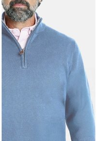 Suéter de cuello con cremallera en azul claro, hecho de un suave tejido de punto. Presenta una textura lisa y un pequeño tirador de cremallera marrón. Lleva encima una camisa rosa con cuello.