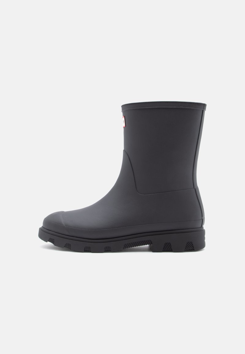 Black rubber ankle boot featuring a smooth finish, textured sole with treads, and a simple design. Red logo tag on the side.