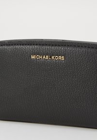 Zwarte leren portemonnee met een textuur, voorzien van een gouden "MICHAEL KORS" logo. Het ontwerp is strak met afgeronde hoeken en zichtbare stiksels.