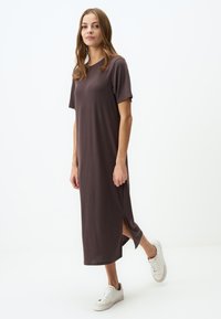 Robe marron, longueur genou avec des manches courtes et des fentes latérales, en tissu doux. Associée à des baskets blanches pour un look décontracté.