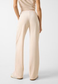 Beige weit geschnittene Hose aus weichem Stoff, mit glatter Textur, elastischem Bund und simplem Design.