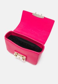 Różowa skórzana torebka o strukturalnym kształcie, z zapięciem na złotą klamrę i czarną etykietą wewnętrzną. Wnętrze nie jest wyłożone.