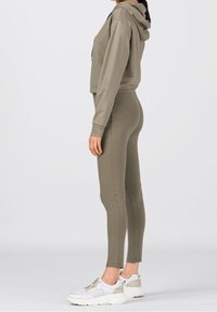 Olivgrön croppad hoodie med dragsko på huvan, tillsammans med matchande figurnära leggings och klumpiga vita sneakers. Slät, elastisk tyg.