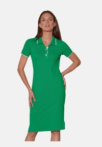 Grünes Polo-Kleid aus Baumwolle mit schlanker Passform. Verfügt über kurze Ärmel, einen Kragen und weiße Akzente entlang des Kragens und der Ärmel.