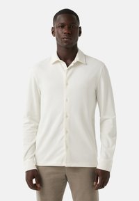 Witte longsleeve shirt gemaakt van zachte stof, met een knoopsluiting aan de voorkant, een spitse kraag en een getailleerde pasvorm. Geen patronen of accenten.