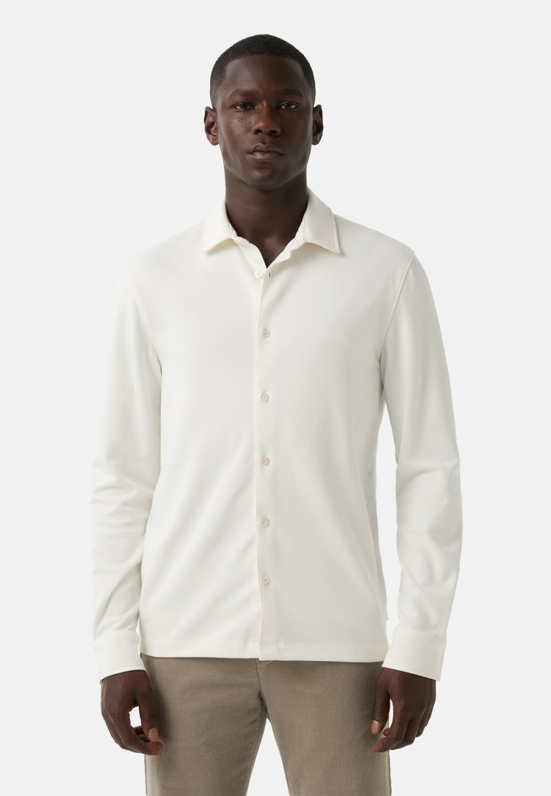 Witte longsleeve shirt gemaakt van zachte stof, met een knoopsluiting aan de voorkant, een spitse kraag en een getailleerde pasvorm. Geen patronen of accenten.