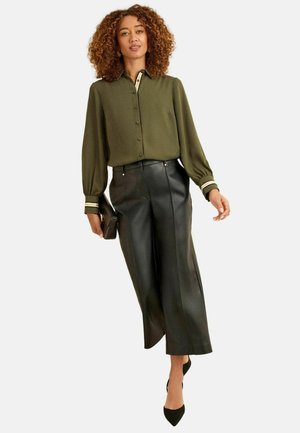 Olivgrüne Knopfbluse mit Streifen an den Bündchen, kombiniert mit hoch taillierten, weit geschnittenen schwarzen Lederhosen und schwarzen spitzen Absätzen.